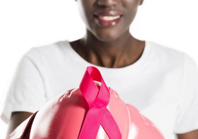 close-up view of young african american woman in boxing gloves holding pink ribbon and smiling at