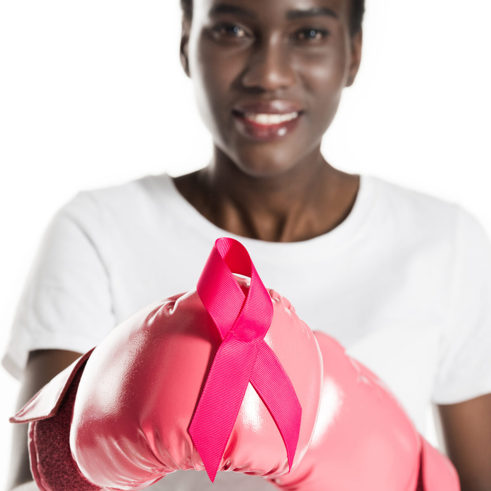 close-up view of young african american woman in boxing gloves holding pink ribbon and smiling at