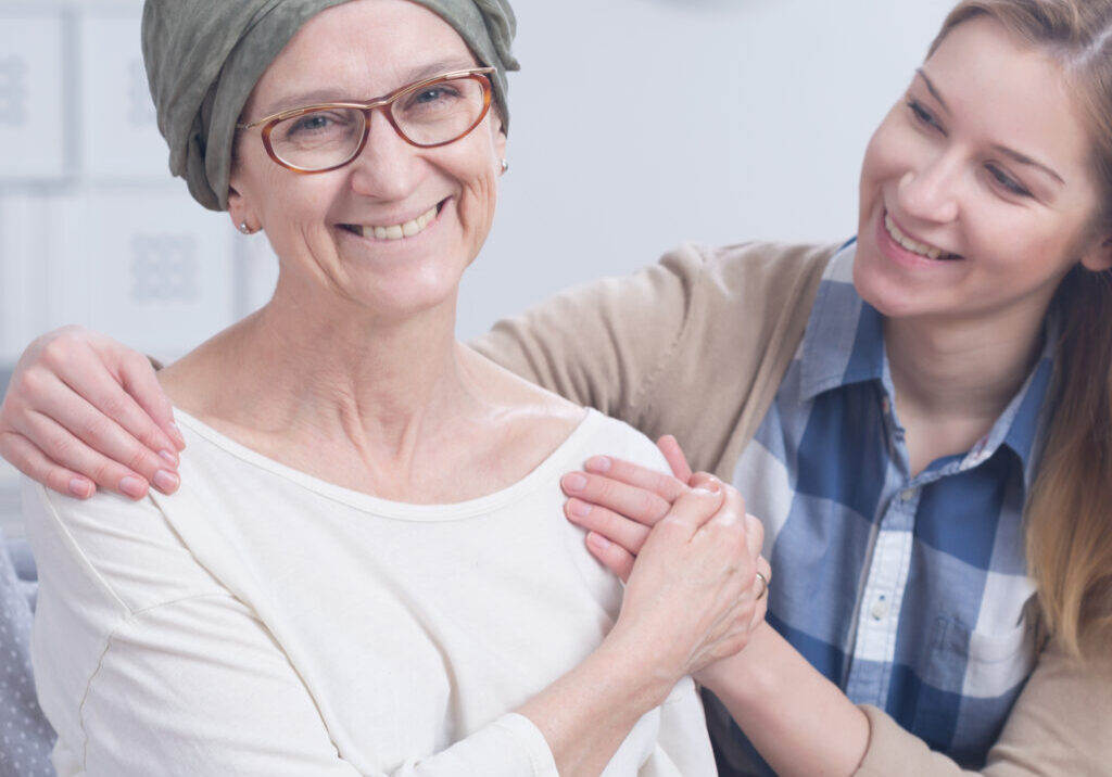 Smiling cancer woman with headscarf embraced by young happy girl