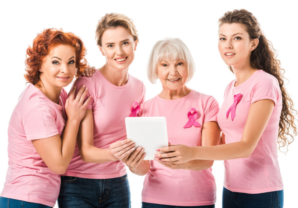 women in pink t-shirts with breast cancer awareness ribbons holding digital tablet and smiling at