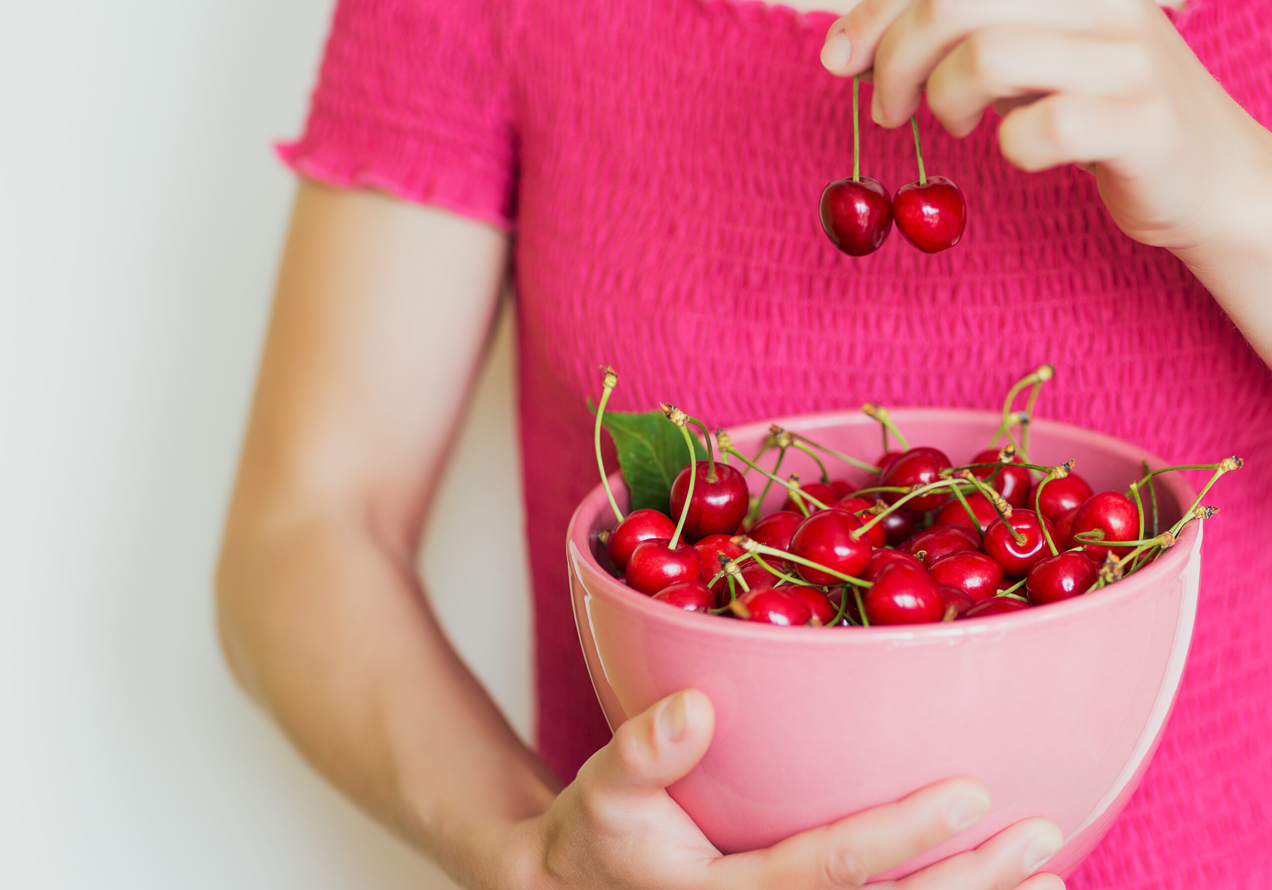 Two cherries in a woman's hand. Young pretty woman in pink dress play with berries.