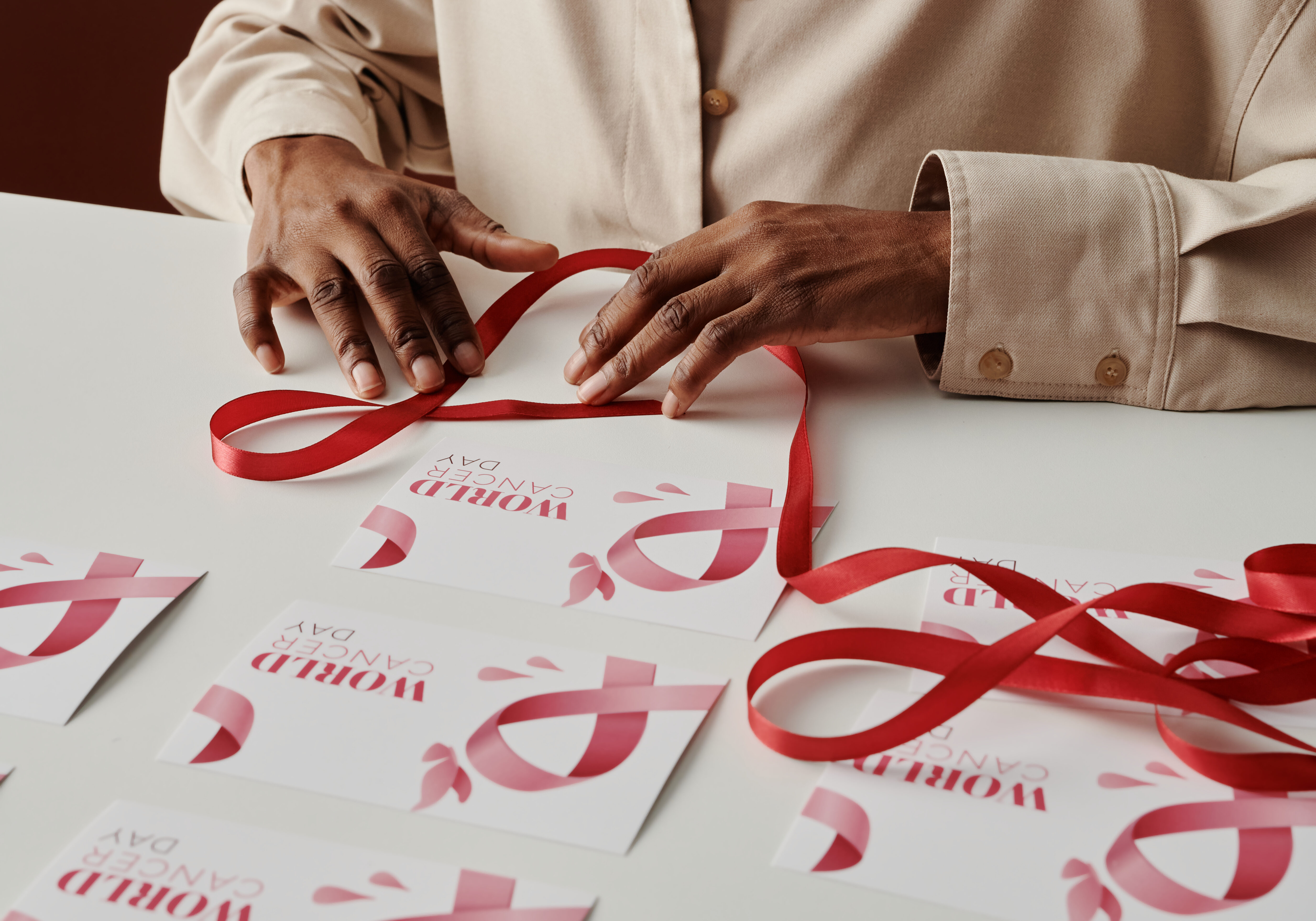 Young unrecognizable African American woman with pink ribbon preparing postcards before world cancer day while sitting by table